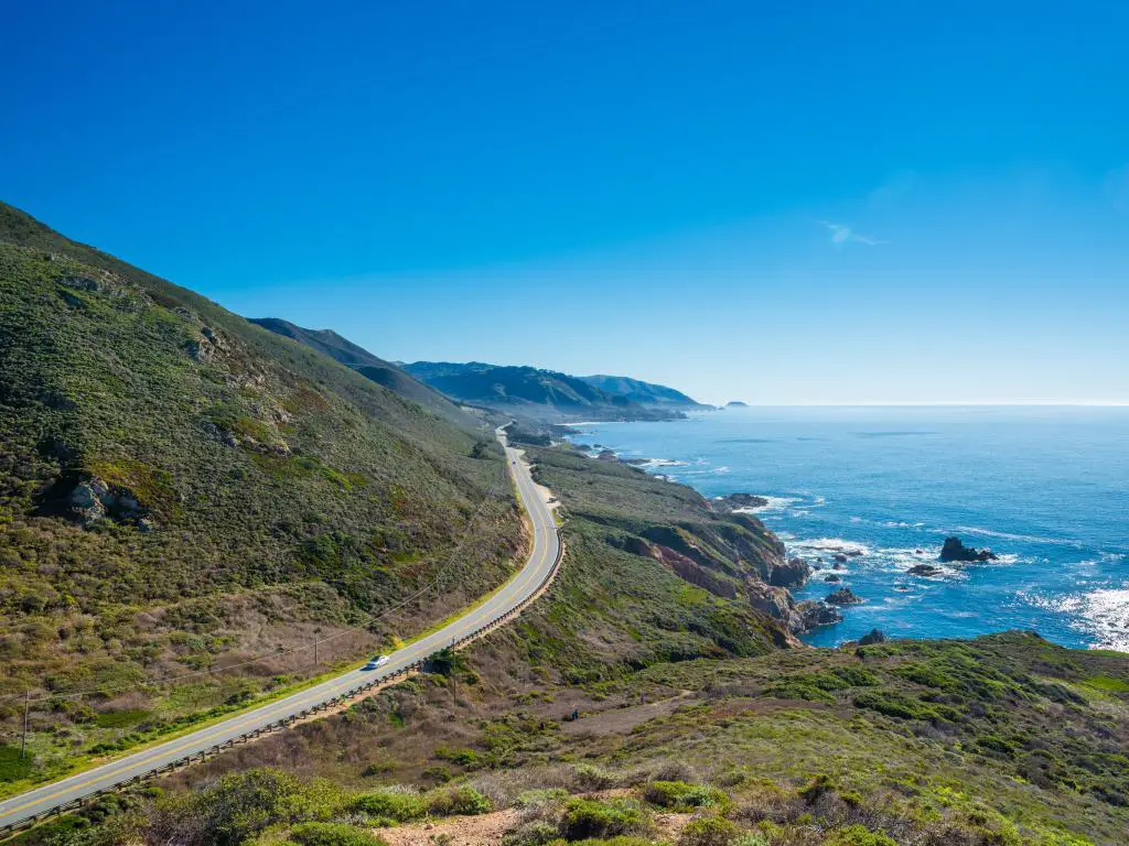 Ruta 1 del estado de California, con una carretera que bordea montañas verdes y el mar azul brillante a la derecha.