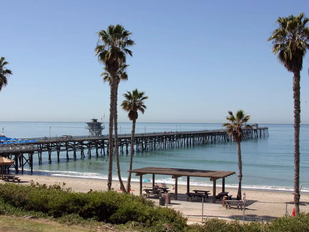 Muelle de San Clemente que se adentra en el mar frente a la costa de California con una playa bordeada de palmeras.