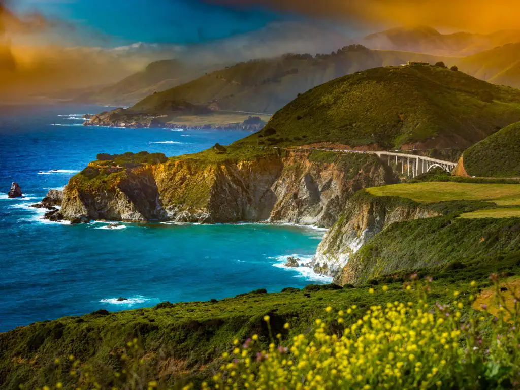 Mar azul vibrante y luz solar dorada con la autopista de la costa del Pacífico que serpentea a lo largo de acantilados rocosos