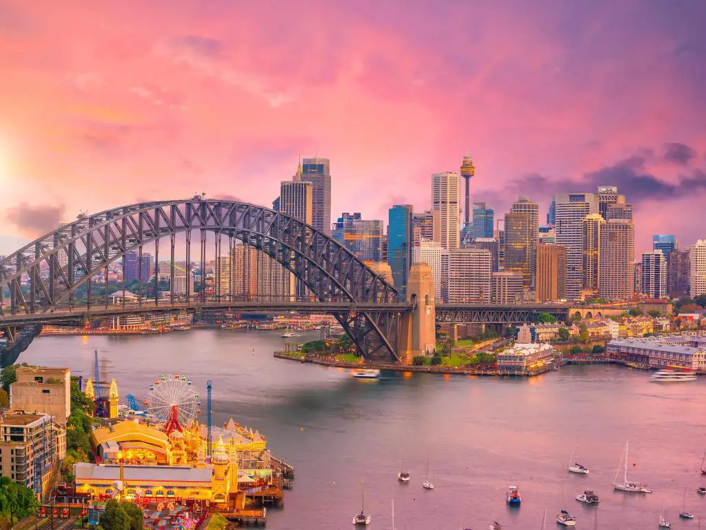 Paisaje urbano con Sydney Harbour Bridge y edificios altos de Sydney vistos a través de una bahía donde muchos botes pequeños están amarrados durante la puesta de sol