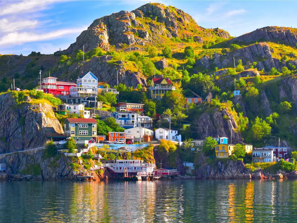 Puerto de St John, Newfoundland, Canadá, con el mar en primer plano, mirando a la comunidad de hermosos edificios de colores en la isla, empinada con rocas y grandes áreas verdes en un día soleado. 