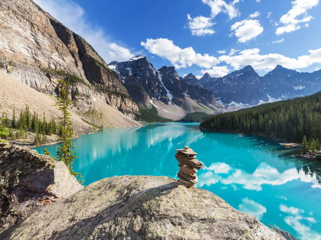 Parque Nacional Banff, Canadá, tomada en el hermoso lago Moraine con rocas en primer plano y el agua turquesa que refleja las montañas nevadas a lo lejos en un día soleado.