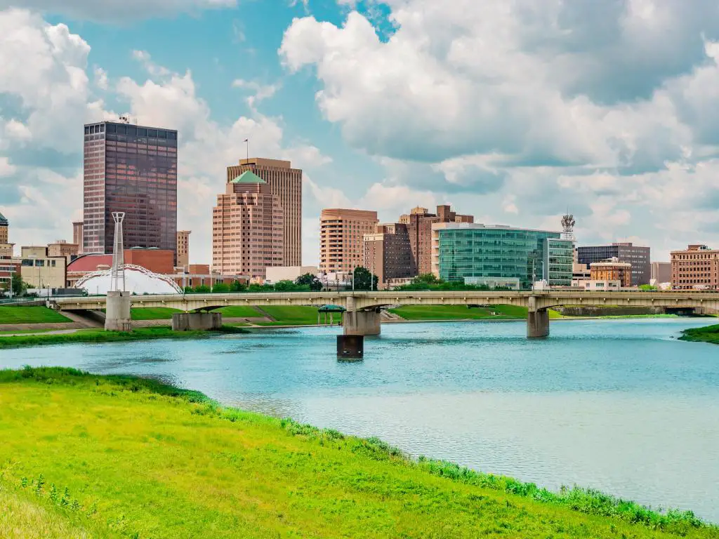 Dayton, Ohio, con el río Miami en primer plano y un puente con los edificios de la ciudad al fondo contra un cielo azul. 