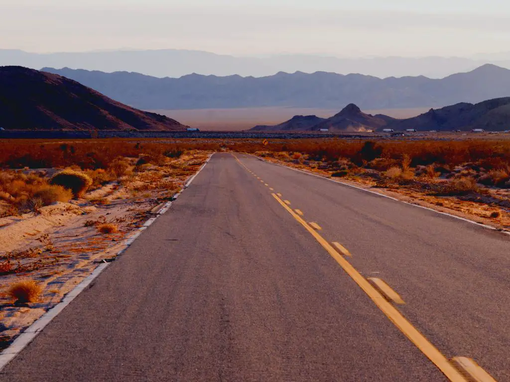 Una Interestatal 40 vacía a lo largo de la Autopista Needles en Mojave National Preserve con vistas a las montañas en una tarde nebulosa.
