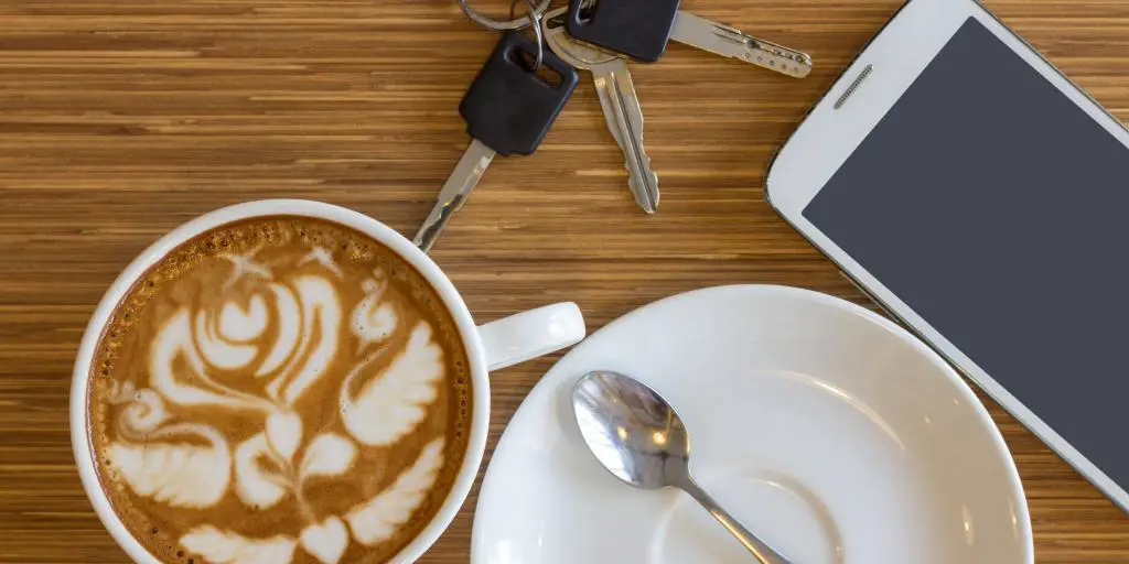 Café, llaves y teléfono móvil sobre una superficie marrón.