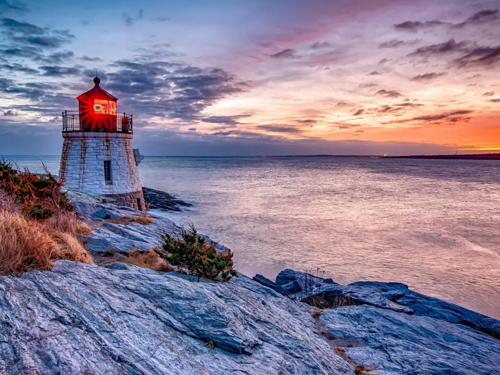 Vibrante puesta de sol sobre el agua con Castle Hill Lighthouse encaramado en el borde del acantilado, Newport, Rhode Island