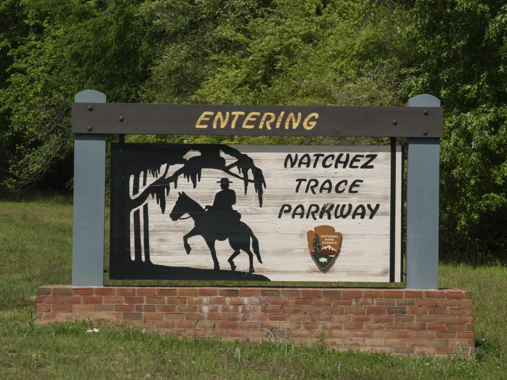 Letrero en la entrada de Natchez Trace Parkway que muestra a un hombre a caballo, con árboles detrás