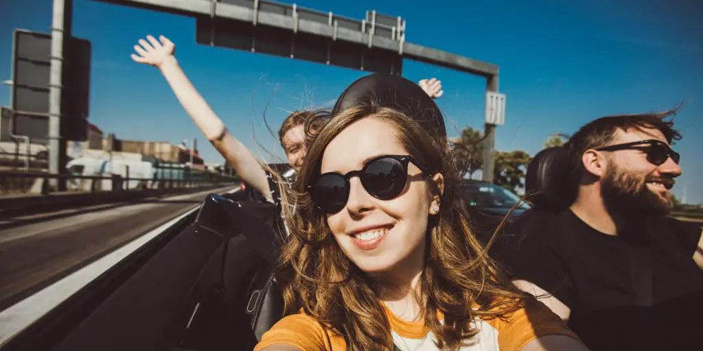 Feliz grupo de amigos tomando selfie cuando viaje por carretera en auto convertible en un día soleado